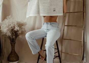 Woman sitting indoors holding a vintage newspaper, creating a dramatic and artistic scene.