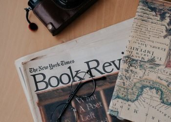 Flat lay of vintage camera, map, and book review on wooden surface.